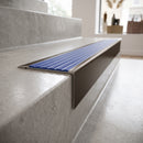Solid Brass Stair Nosing 71mm Tread Square Front Slimline in Antique Bronze finish with Mid Blue Castellated insert fitted on a retail store staircase with polished concrete treads