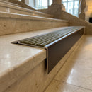 Solid Brass Stair Nosing 71mm Tread Square Front Slimline in Antique Bronze finish with Olive Castellated insert fitted on a hotel lobby staircase with cream marble treads
