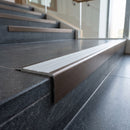 Solid Brass Stair Nosing 71mm Tread Square Front Slimline in Antique Bronze finish with Polar Grey Castellated insert fitted on a public building staircase with dark stone treads