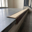 Solid Brass Stair Nosing 71mm Tread Square Front Slimline in Antique Bronze finish with Porth Stone Smooth Textured insert fitted on a public building staircase with dark stone treads