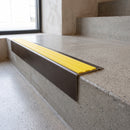 Solid Brass Stair Nosing 71mm Tread Square Front Slimline in Antique Bronze finish with Yellow Castellated insert fitted on a retail store staircase with polished concrete treads