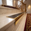 Solid Brass Stair Nosing 71mm Tread Square Front Slimline in Polished Brass finish with Antique Bronze insert fitted on a hotel lobby staircase with cream marble treads