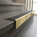 Solid Brass Stair Nosing 71mm Tread Square Front Slimline in Polished Brass finish with Black Olympic Grip insert fitted on a public building staircase with dark stone treads