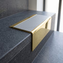 Solid Brass Stair Nosing 71mm Tread Square Front Slimline in Polished Brass finish with Light Grey Smooth Textured insert fitted on a public building staircase with dark stone treads