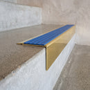Solid Brass Stair Nosing 71mm Tread Square Front Slimline in Polished Brass finish with Mid Blue Castellated insert fitted on a retail store staircase with polished concrete treads