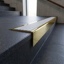 Solid Brass Stair Nosing 71mm Tread Square Front Slimline in Polished Brass finish with Polar Grey Castellated insert fitted on a public building staircase with dark stone treads