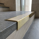 Solid Brass Stair Nosing 71mm Tread Square Front Slimline in Polished Brass finish with Porth Stone Smooth Textured insert fitted on a public building staircase with dark stone treads