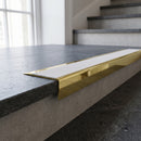 Solid Brass Stair Nosing 71mm Tread Square Front Slimline in Polished Brass finish with White Castellated insert fitted on a public building staircase with dark stone treads