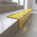 Solid Brass Stair Nosing 71mm Tread Square Front Slimline in Polished Brass finish with Yellow Castellated insert fitted on a retail store staircase with polished concrete treads