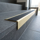 Solid Brass Stair Nosing 71mm Tread Square Front Slimline in Satin Brass finish with Black Olympic Grip insert fitted on a public building staircase with dark stone treads