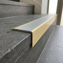 Solid Brass Stair Nosing 71mm Tread Square Front Slimline in Satin Brass finish with Light Grey Smooth Textured insert fitted on a public building staircase with dark stone treads