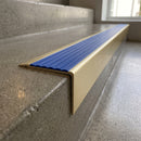 Solid Brass Stair Nosing 71mm Tread Square Front Slimline in Satin Brass finish with Mid Blue Castellated insert fitted on a retail store staircase with polished concrete treads