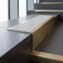 Solid Brass Stair Nosing 71mm Tread Square Front Slimline in Satin Brass finish with Polar Grey Castellated insert fitted on a public building staircase with dark stone treads