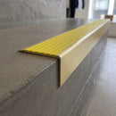 Solid Brass Stair Nosing 71mm Tread Square Front Slimline in Satin Brass finish with Yellow Castellated insert fitted on a retail store staircase with polished concrete treads