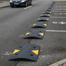 Black rubber modular speed bump sections installed across a tarmac car park driveway entrance