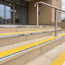 Mirror polished silver 56mm square aluminium stair nosing with brimstone (safety yellow) exterior grip insert on buff concrete entrance steps outside a health centre
