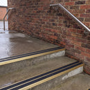Square edge aluminium stair nosing with black gritted exterior grip insert in satin gold finish fitted on covered external concrete steps