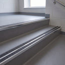 Square edge aluminium stair nosing with twin dark charcoal Mor Grip inserts in bright polished finish fitted on a school corridor stair finished in grey sheet vinyl