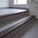 Square edge aluminium stair nosing with twin dark charcoal Mor Grip inserts in dark bronze finish fitted on a school corridor stair finished in grey sheet vinyl