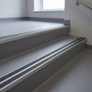 Square edge aluminium stair nosing with twin dark charcoal Mor Grip inserts in mill finish finish fitted on a school corridor stair finished in grey sheet vinyl