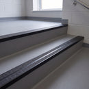 Square edge aluminium stair nosing with twin dark charcoal Mor Grip inserts in satin black finish fitted on a school corridor stair finished in grey sheet vinyl