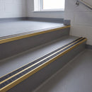 Square edge aluminium stair nosing with twin dark charcoal Mor Grip inserts in satin gold finish fitted on a school corridor stair finished in grey sheet vinyl