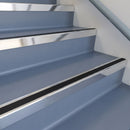 Square DDA aluminium stair nosing with black insert in bright polished finish fitted on a public building stair with blue-grey safety vinyl