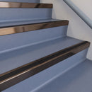 Square DDA aluminium stair nosing with black insert in dark bronze finish fitted on a public building stair with blue-grey safety vinyl