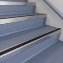Square DDA aluminium stair nosing with black insert in mill finish fitted on a public building stair with blue-grey safety vinyl