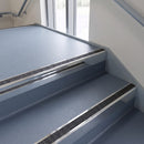 Square edge aluminium stair nosing with a dark charcoal Mor Grip insert in bright polished finish fitted on a public building stair finished in blue-grey safety vinyl