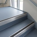Square edge aluminium stair nosing with a dark charcoal Mor Grip insert in mill finish finish fitted on a public building stair finished in blue-grey safety vinyl