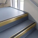 Square edge aluminium stair nosing with a dark charcoal Mor Grip insert in satin gold finish fitted on a public building stair finished in blue-grey safety vinyl
