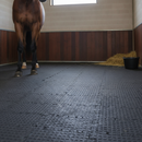 Horse standing on black interlocking rubber stable matting in a stable with straw and a water bucket