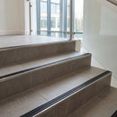 Stainless steel tile-in stair nosing with GS Black RAL 9011 ribbed insert on pale grey porcelain stairs