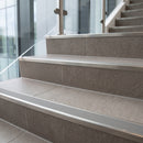 Stainless steel tile-in stair nosing with G Grey RAL 7030 ribbed insert forming the step edge on a tiled office stairwell