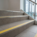 Stainless steel tile-in stair nosing with CG Yellow RAL 1021 ribbed insert on a commercial tiled staircase