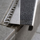 Close-up of the anti-slip tread texture and brushed steel edge of a stair nosing bedded on a tiled step