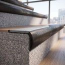 Solid brass bullnose stair nosing in Antique Bronze finish with Polar Grey Castellated anti-slip infill fitted to a stair tread in a commercial stairwell