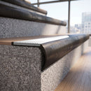 Solid brass bullnose stair nosing in Antique Bronze finish with White Castellated anti-slip infill fitted to a stair tread in a commercial stairwell