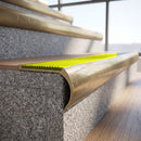 Solid brass bullnose stair nosing with Yellow Castellated anti-slip infill fitted to a stair tread in a commercial stairwell