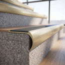 Solid brass bullnose stair nosing in Satin Brass finish with Light Grey Castellated anti-slip infill fitted to a stair tread in a commercial stairwell