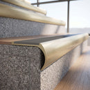 Solid brass bullnose stair nosing in Satin Brass finish with Light Grey Smooth Textured anti-slip infill fitted to a stair tread in a commercial stairwell