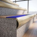 Solid brass bullnose stair nosing in Satin Brass finish with Mid Blue Castellated anti-slip infill fitted to a stair tread in a commercial stairwell