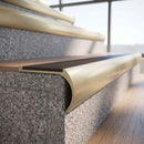 Solid brass bullnose stair nosing in Satin Brass finish with Peat Castellated anti-slip infill fitted to a stair tread in a commercial stairwell