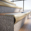 Solid brass bullnose stair nosing in Satin Brass finish with Polar Grey Castellated anti-slip infill fitted to a stair tread in a commercial stairwell