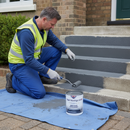Worker in hi-vis applying mid grey anti-slip step paint to concrete steps outside a UK home