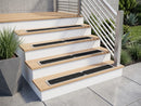 Black carbide treadplates fitted to four oak-topped white steps beside a slatted metal handrail and planted courtyard
