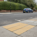 Buff tactile paving blister slabs set into a pavement at a dropped kerb crossing point on a UK residential street