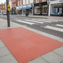 Red tactile paving blister slabs set into a pavement at a controlled pelican crossing on a UK high street