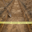 Yellow underground warning tape laid across the bottom of an open excavation trench above a buried electric cable